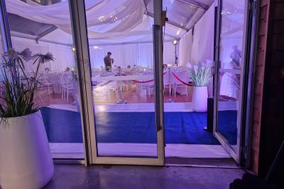 Salle moderne avec tables hautes blanches, éclairage coloré et murs vitrés, prête pour un événement.