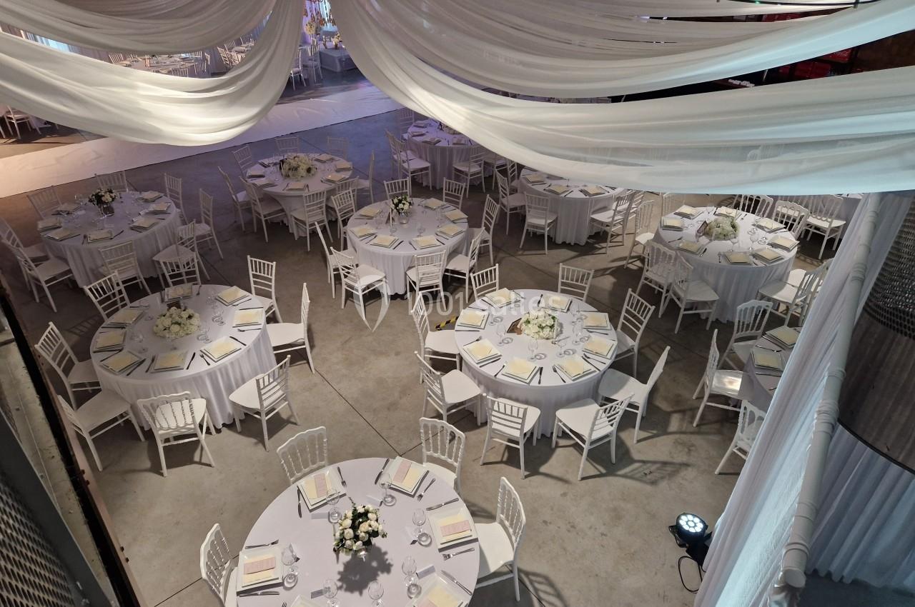 Salle de réception décorée avec des tables rondes, nappes blanches, chaises assorties et centres de table floraux.