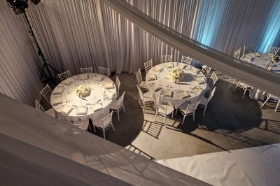 Salle moderne avec tables hautes blanches, éclairage coloré et murs vitrés, prête pour un événement.