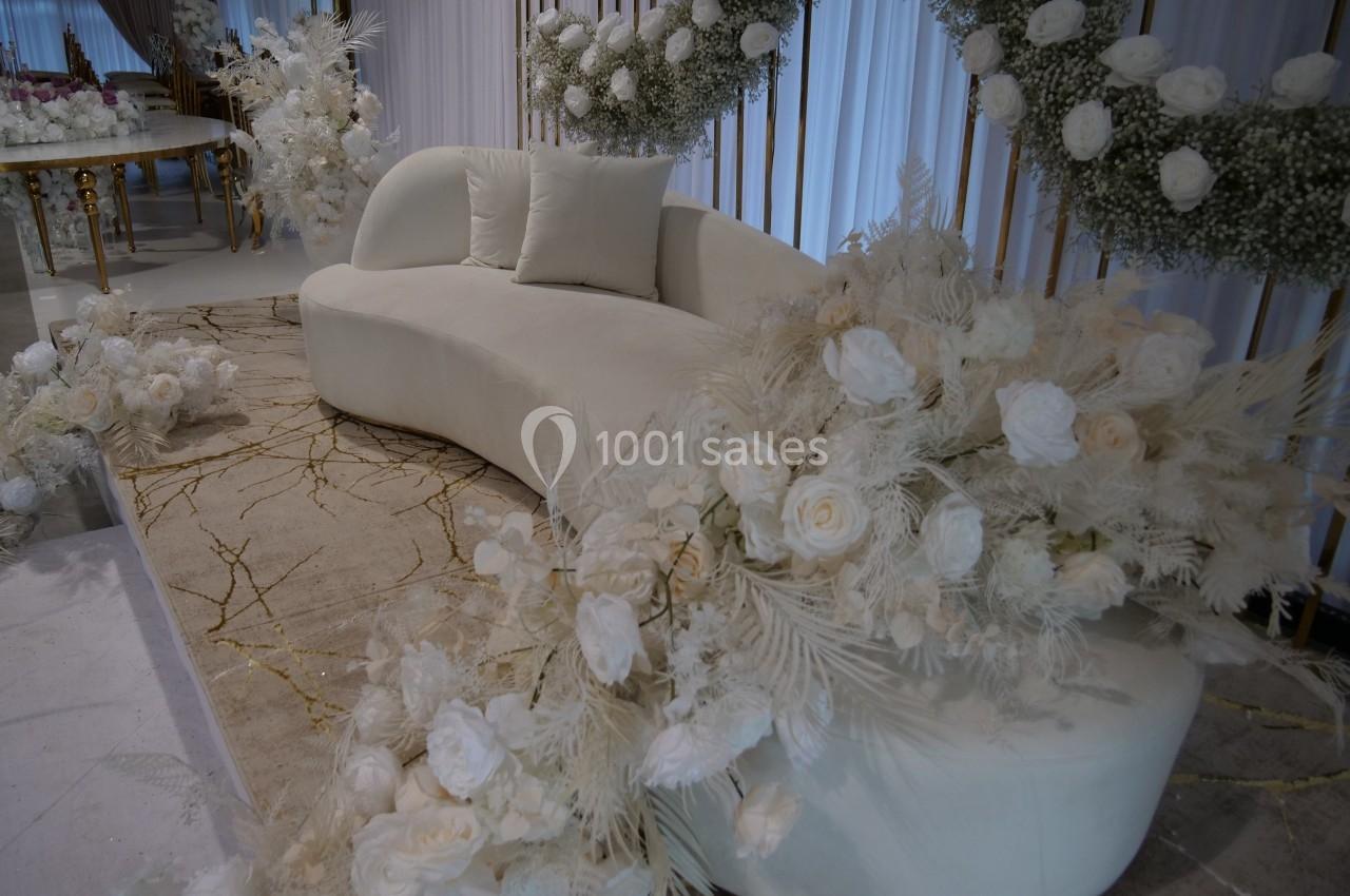 Canapé blanc entouré de décorations florales blanches et de feuillages, dans un cadre élégant et lumineux.