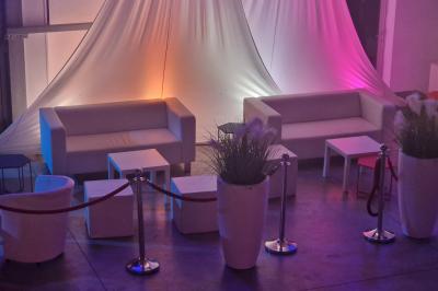 Salle moderne avec tables hautes blanches, éclairage coloré et murs vitrés, prête pour un événement.