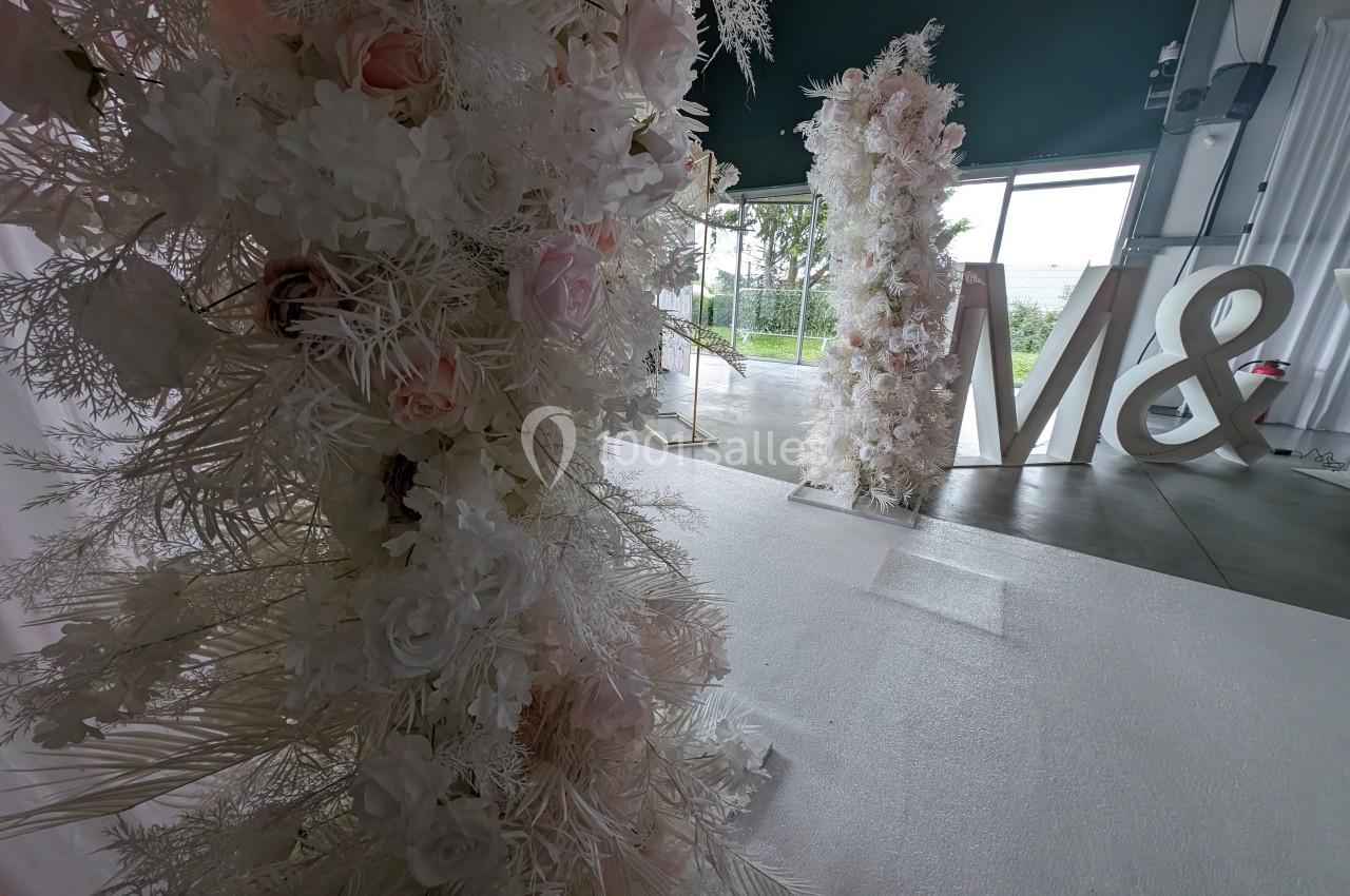 Décor floral blanc et rose avec des lettres géantes ’M &’ dans une salle lumineuse donnant sur un extérieur verdoyant.