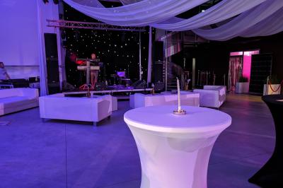 Salle moderne avec tables hautes blanches, éclairage coloré et murs vitrés, prête pour un événement.