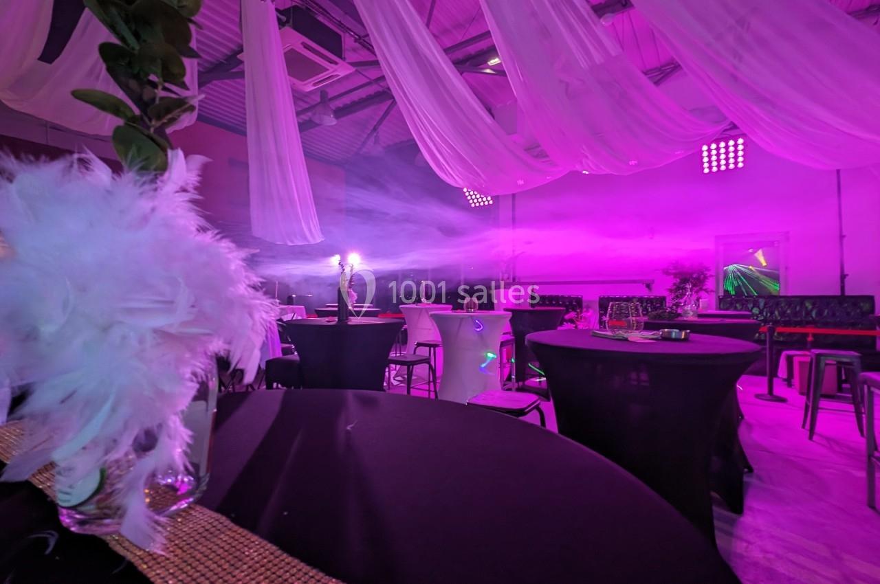 Salle de réception décorée avec des tables noires, des voilages suspendus et un éclairage rose tamisé.