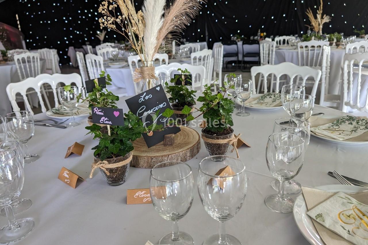 Table décorée pour un événement avec nappes blanches, plantes en centre de table et vaisselle élégante.