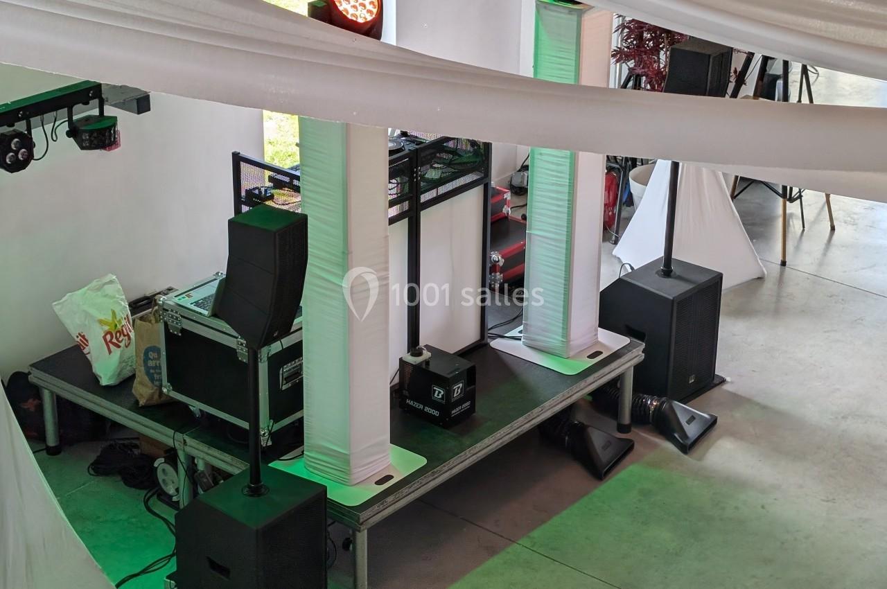 Équipement de sonorisation et éclairage installé sur une petite scène dans un espace intérieur décoré de voilages blancs.