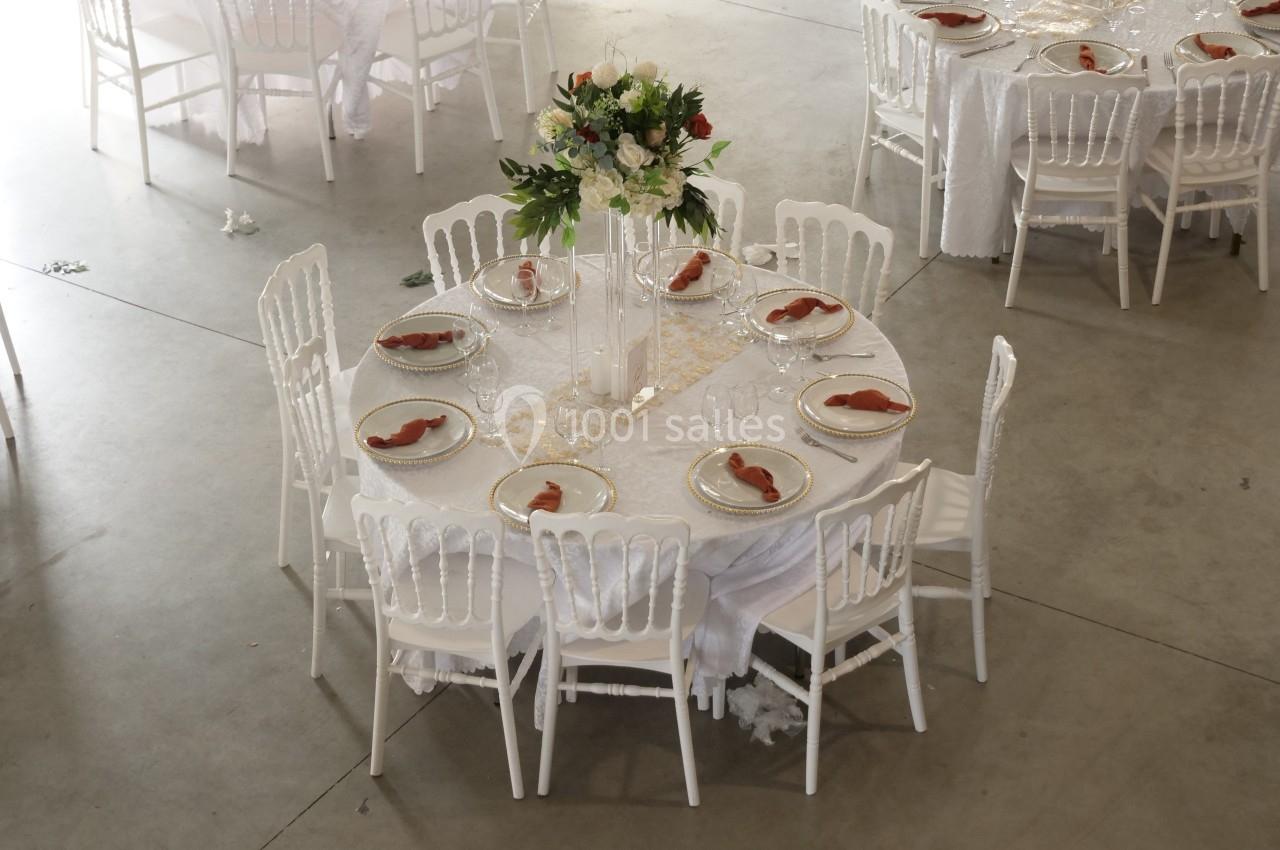 Table ronde décorée pour un événement, avec nappes blanches, vaisselle élégante et centre de table floral.