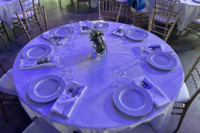 Salle moderne avec tables hautes blanches, éclairage coloré et murs vitrés, prête pour un événement.
