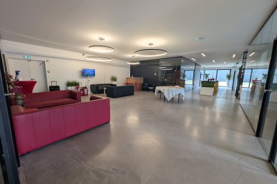 Salle moderne avec tables hautes blanches, éclairage coloré et murs vitrés, prête pour un événement.