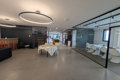 Salle moderne avec tables hautes blanches, éclairage coloré et murs vitrés, prête pour un événement.