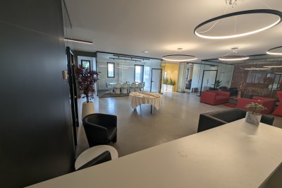 Salle moderne avec tables hautes blanches, éclairage coloré et murs vitrés, prête pour un événement.