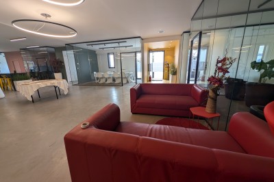 Salle moderne avec tables hautes blanches, éclairage coloré et murs vitrés, prête pour un événement.