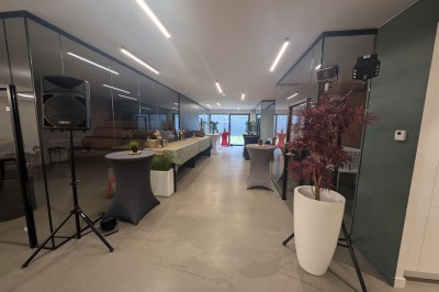 Salle moderne avec tables hautes blanches, éclairage coloré et murs vitrés, prête pour un événement.