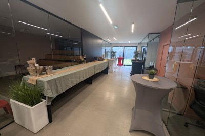 Salle moderne avec tables hautes blanches, éclairage coloré et murs vitrés, prête pour un événement.