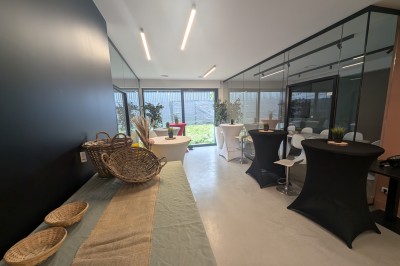 Salle moderne avec tables hautes blanches, éclairage coloré et murs vitrés, prête pour un événement.