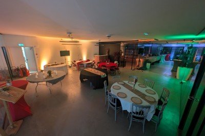 Salle moderne avec tables hautes blanches, éclairage coloré et murs vitrés, prête pour un événement.