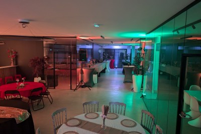 Salle moderne avec tables hautes blanches, éclairage coloré et murs vitrés, prête pour un événement.