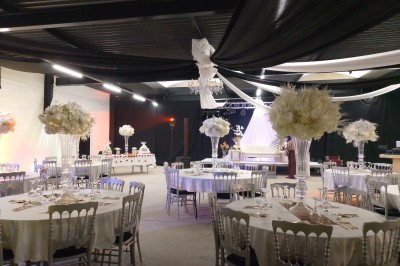 Salle moderne avec tables hautes blanches, éclairage coloré et murs vitrés, prête pour un événement.