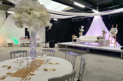 Salle moderne avec tables hautes blanches, éclairage coloré et murs vitrés, prête pour un événement.
