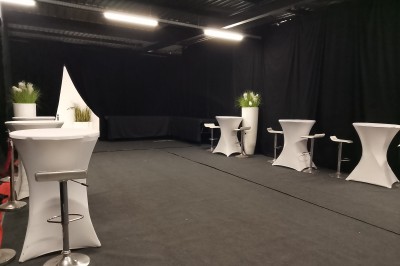 Salle moderne avec tables hautes blanches, éclairage coloré et murs vitrés, prête pour un événement.