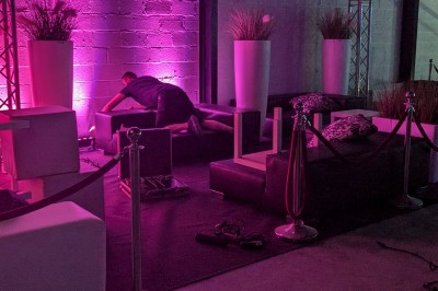 Salle moderne avec tables hautes blanches, éclairage coloré et murs vitrés, prête pour un événement.