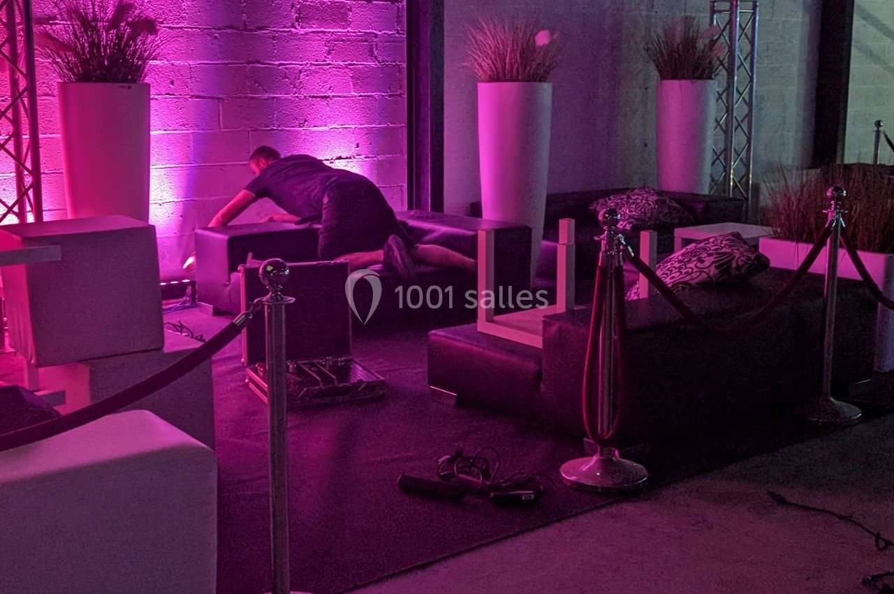 Un homme ajuste un canapé dans un espace intérieur décoré avec des lumières roses et des plantes en pots.