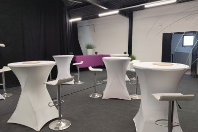 Salle moderne avec tables hautes blanches, éclairage coloré et murs vitrés, prête pour un événement.