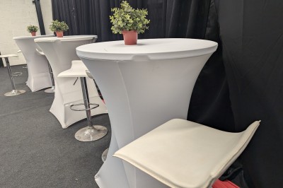 Salle moderne avec tables hautes blanches, éclairage coloré et murs vitrés, prête pour un événement.