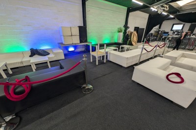 Salle moderne avec tables hautes blanches, éclairage coloré et murs vitrés, prête pour un événement.