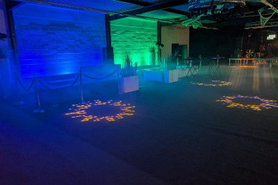 Salle moderne avec tables hautes blanches, éclairage coloré et murs vitrés, prête pour un événement.