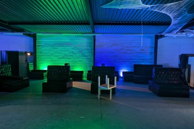 Salle moderne avec tables hautes blanches, éclairage coloré et murs vitrés, prête pour un événement.