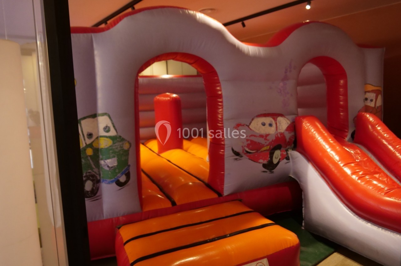 Structure gonflable colorée avec toboggan et illustrations de voitures, située dans un espace intérieur.