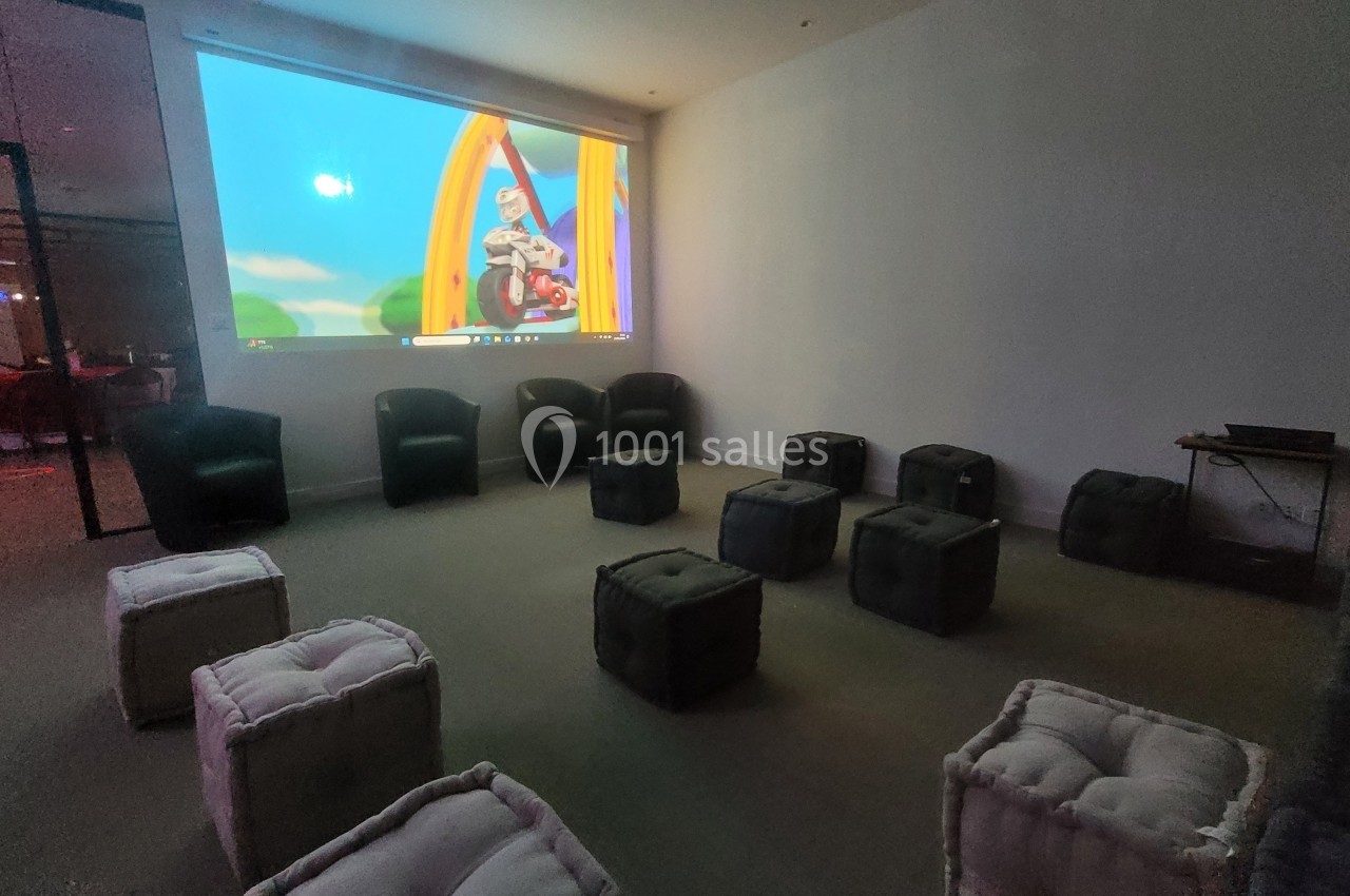 Salle sombre avec des poufs et fauteuils disposés devant un écran projetant un dessin animé coloré.