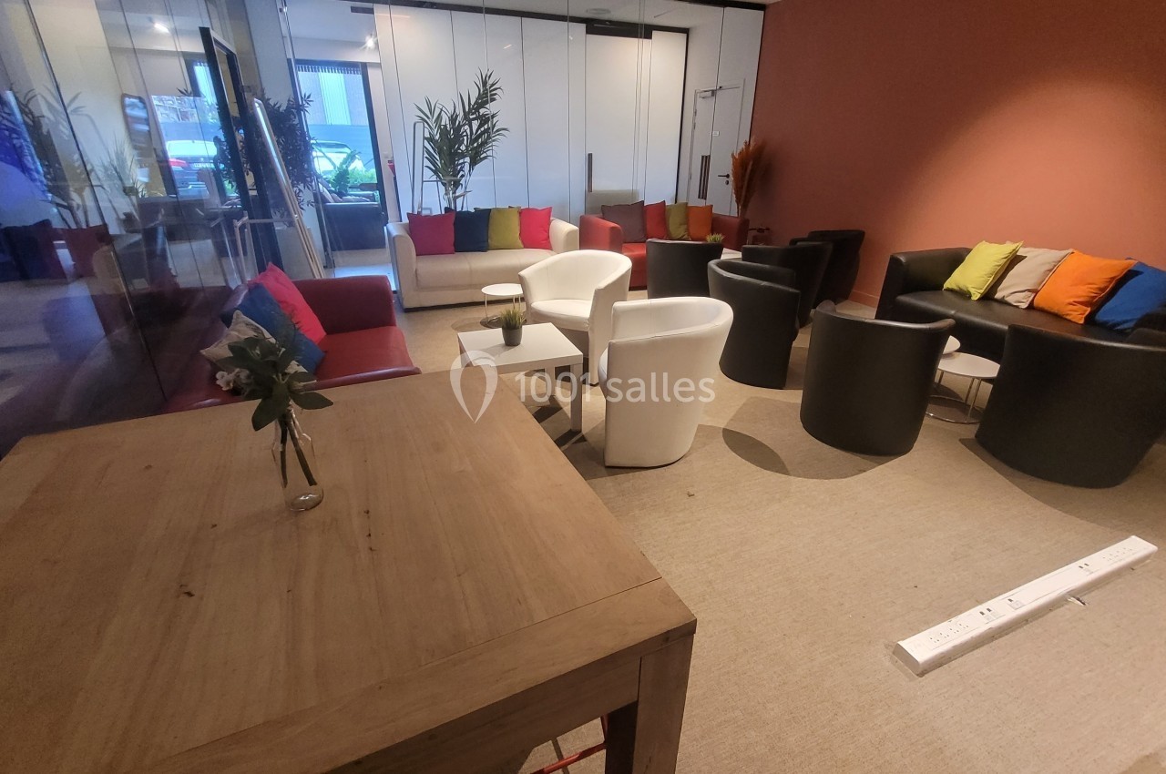 Salle de réunion avec canapés colorés, fauteuils noirs et blancs, table en bois et murs vitrés.