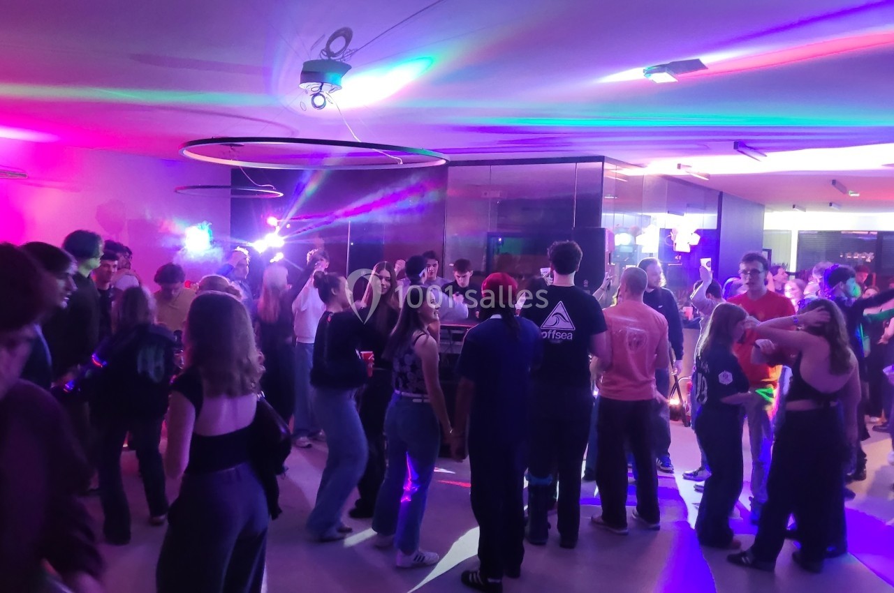 Groupe de personnes dans une salle éclairée par des lumières colorées, dansant et socialisant.