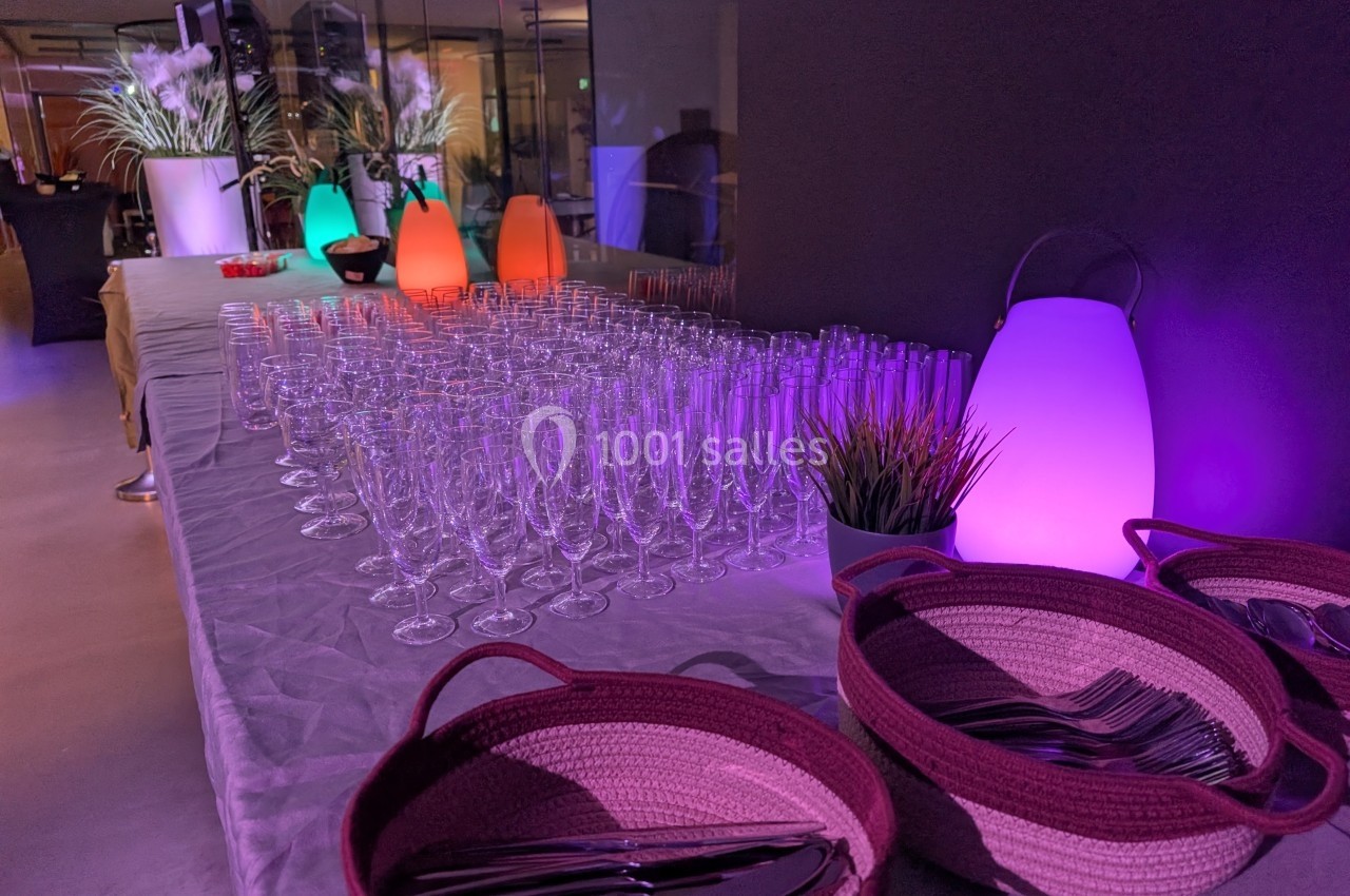 Table dressée avec des verres à pied, paniers contenant des couverts et éclairage coloré dans une ambiance tamisée.
