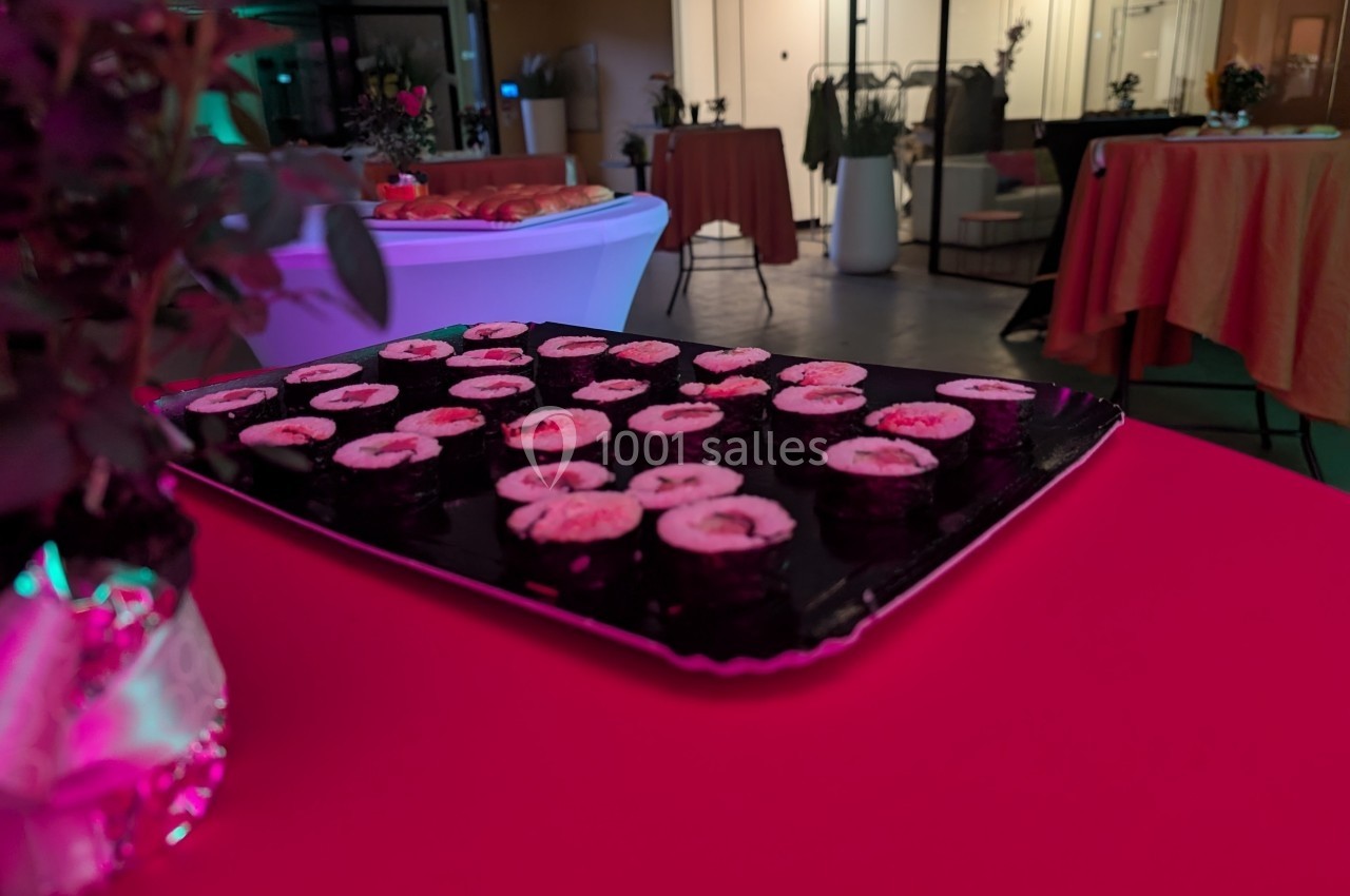 Plateau de sushis disposé sur une table rouge dans une salle éclairée avec des tables et des plantes en arrière-plan.