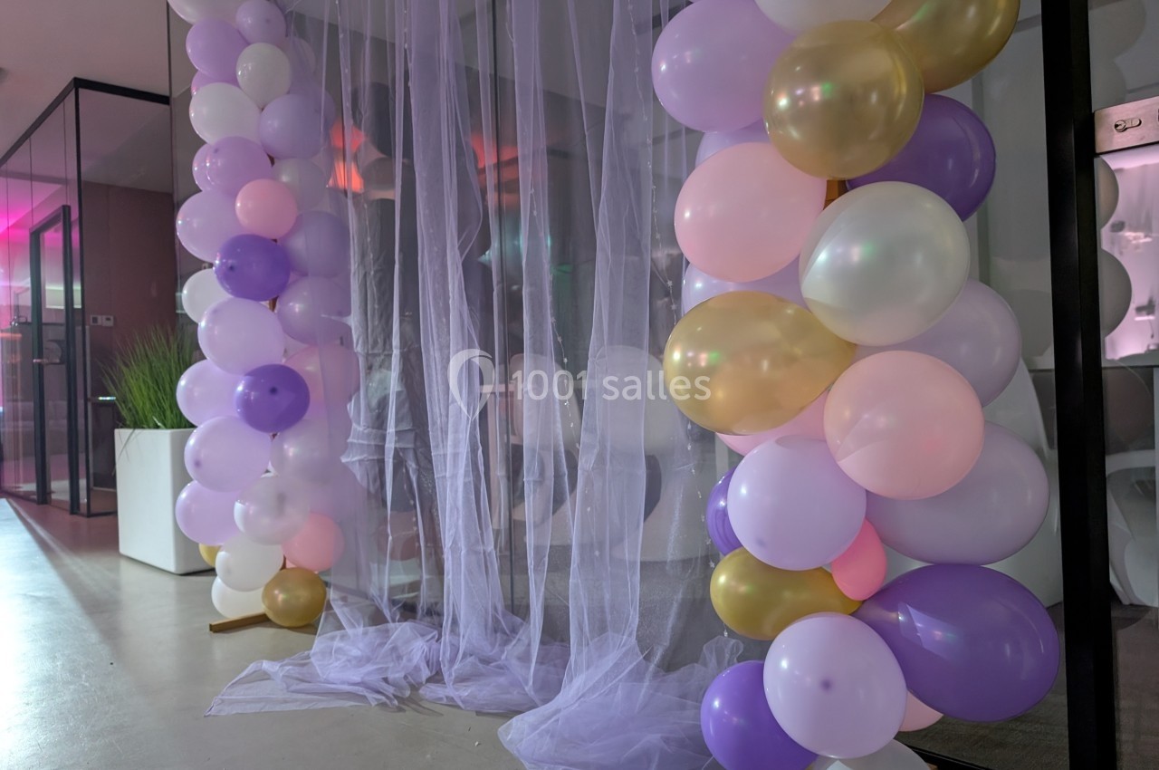 Décoration avec arche de ballons pastel et dorés entourant un voile translucide dans un espace intérieur moderne.