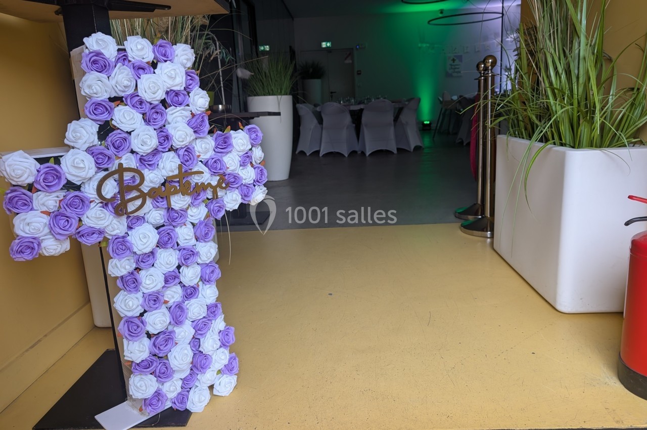 Croix décorative en fleurs violettes et blanches près d'une entrée menant à une salle éclairée en vert.