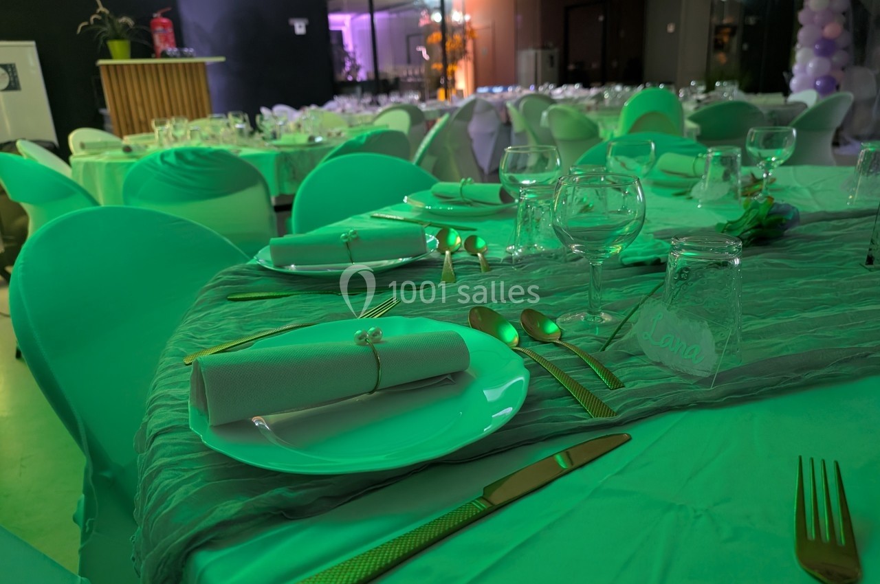 Tables élégamment dressées avec nappes vertes, couverts dorés, verres et serviettes pliées dans une salle de réception.