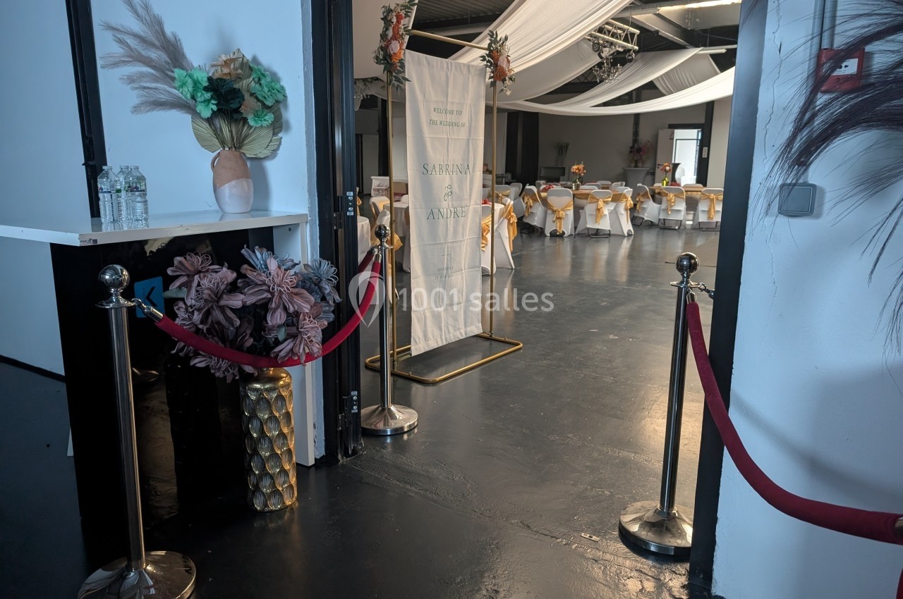 Salle de réception décorée avec des tables dressées, des chaises ornées de rubans dorés et des drapés suspendus.
