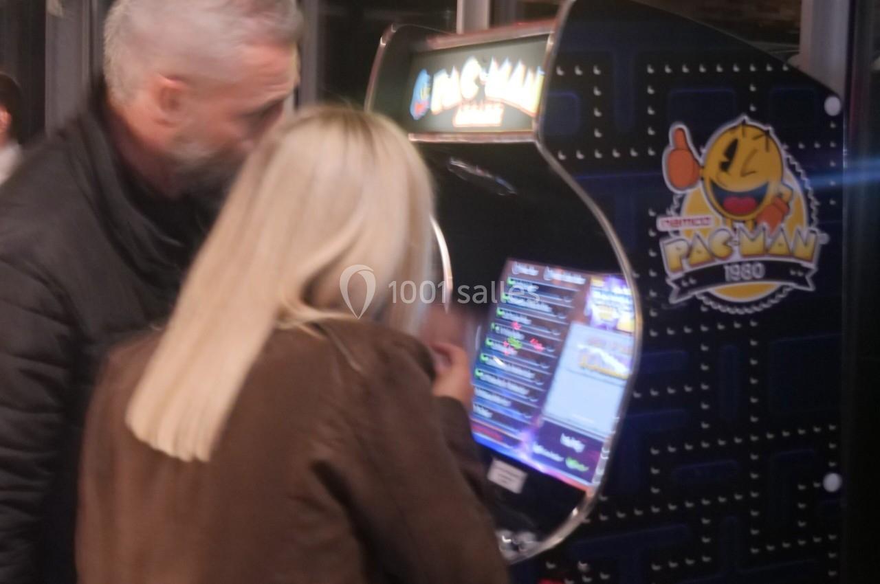Un homme et une femme jouent sur une borne d'arcade rétro Pac-Man dans un espace intérieur.