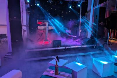 Un grand groupe de jeunes assis dehors sur un sol en béton, près de bâtiments sous un ciel nuageux.