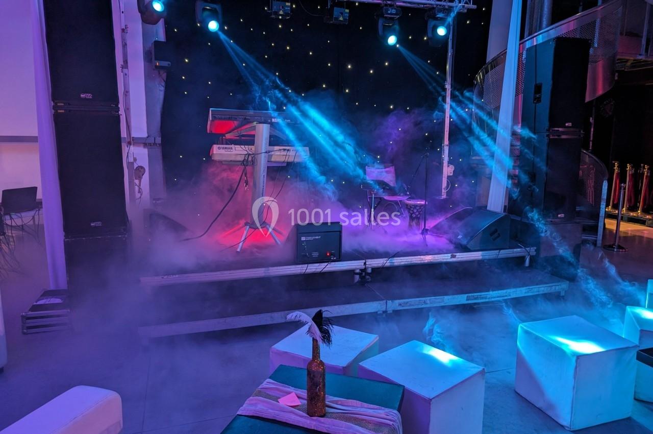 Scène de concert avec claviers, éclairage coloré et fumée, entourée de sièges cubiques dans une ambiance intimiste.