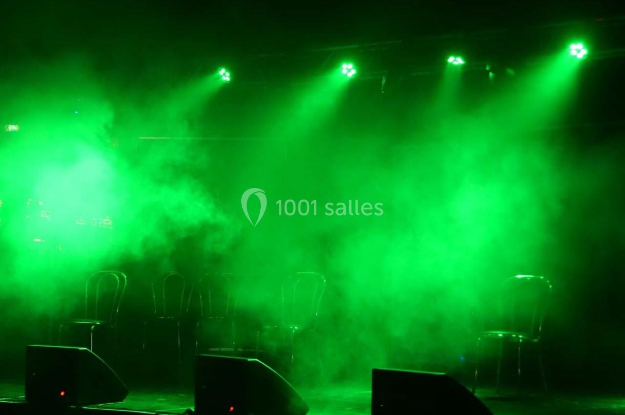 Quatre chaises vides sur une scène enveloppée de lumière verte et de fumée.