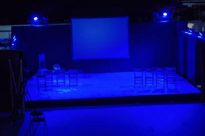 Un grand groupe de jeunes assis dehors sur un sol en béton, près de bâtiments sous un ciel nuageux.
