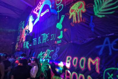 Un grand groupe de jeunes assis dehors sur un sol en béton, près de bâtiments sous un ciel nuageux.