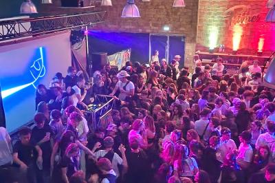 Un grand groupe de jeunes assis dehors sur un sol en béton, près de bâtiments sous un ciel nuageux.
