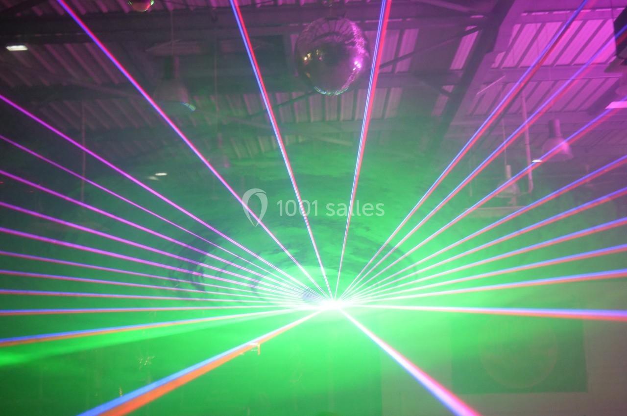 Faisceau de lumières laser multicolores projeté dans une salle sombre avec un plafond métallique visible.