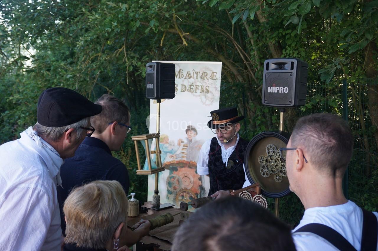 Un homme en costume anime un atelier artisanal en plein air devant un petit groupe de personnes.